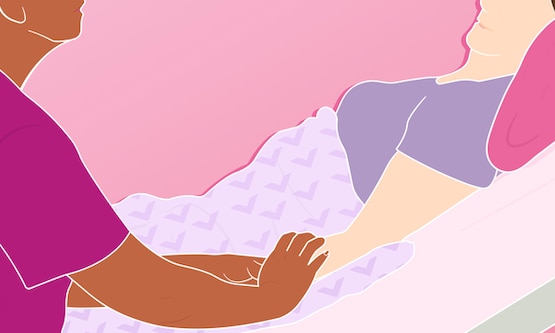 A patient lying down in a hospital bed with their loved one at their side holding their hand.