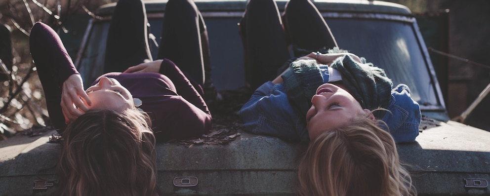 Image of two girls lying on a car talking to each other about their emotions - Libresse