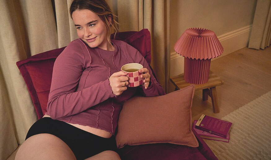 En tenåring som ligger i en lenestol og har på seg en svart menstruse fra Libresse. Menstrusen tar hånd om mensen i opptil 12 timer.