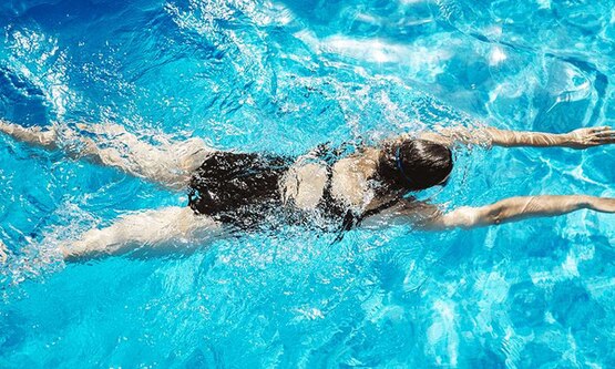 Woman swimming in a pool in swimming costume and goggles while she’s on her period.